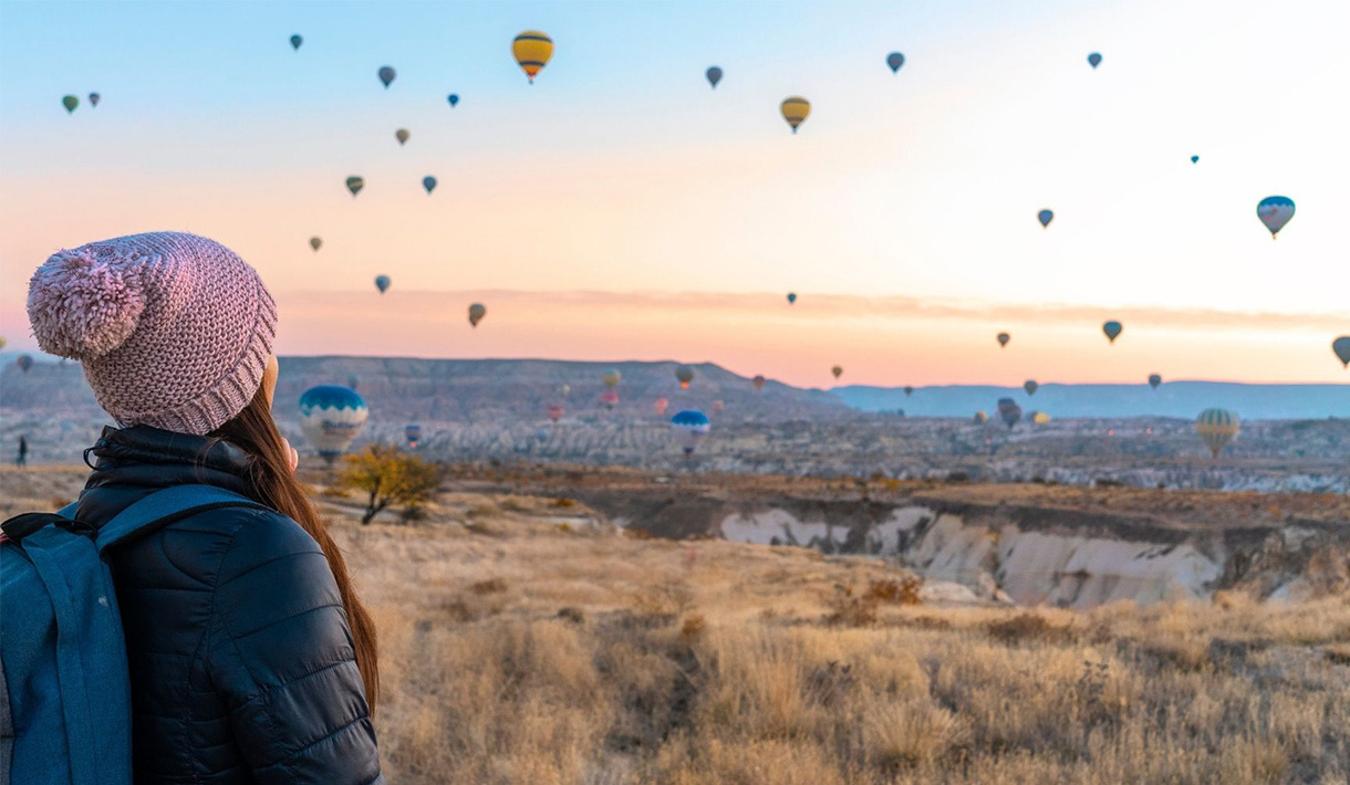Eine Frau schaut zu wie viele Heißluftballons am Horizont aufsteigen.